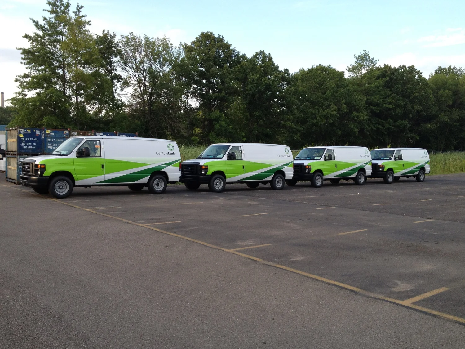 Four white CenturyLink service vans with matching green fleet graphics
