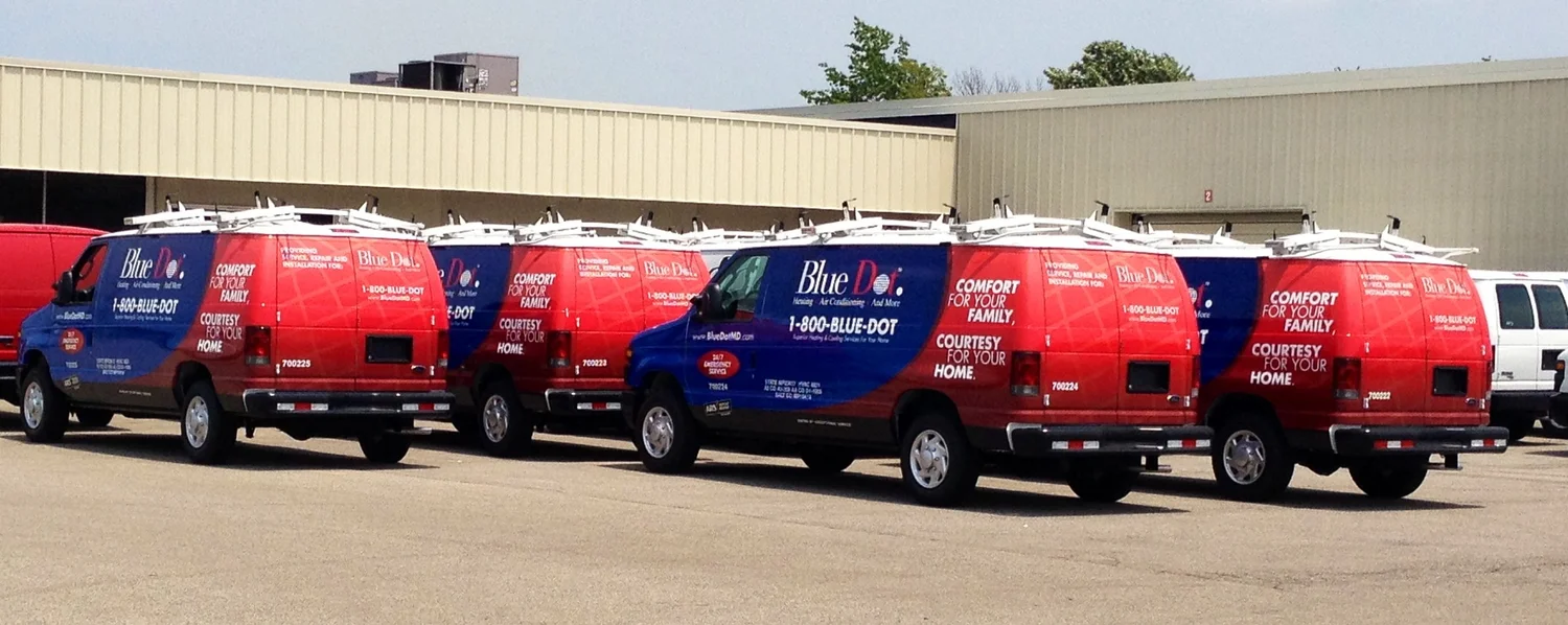 A fleet of red and blue Blue Dot service vans with coordinated wraps